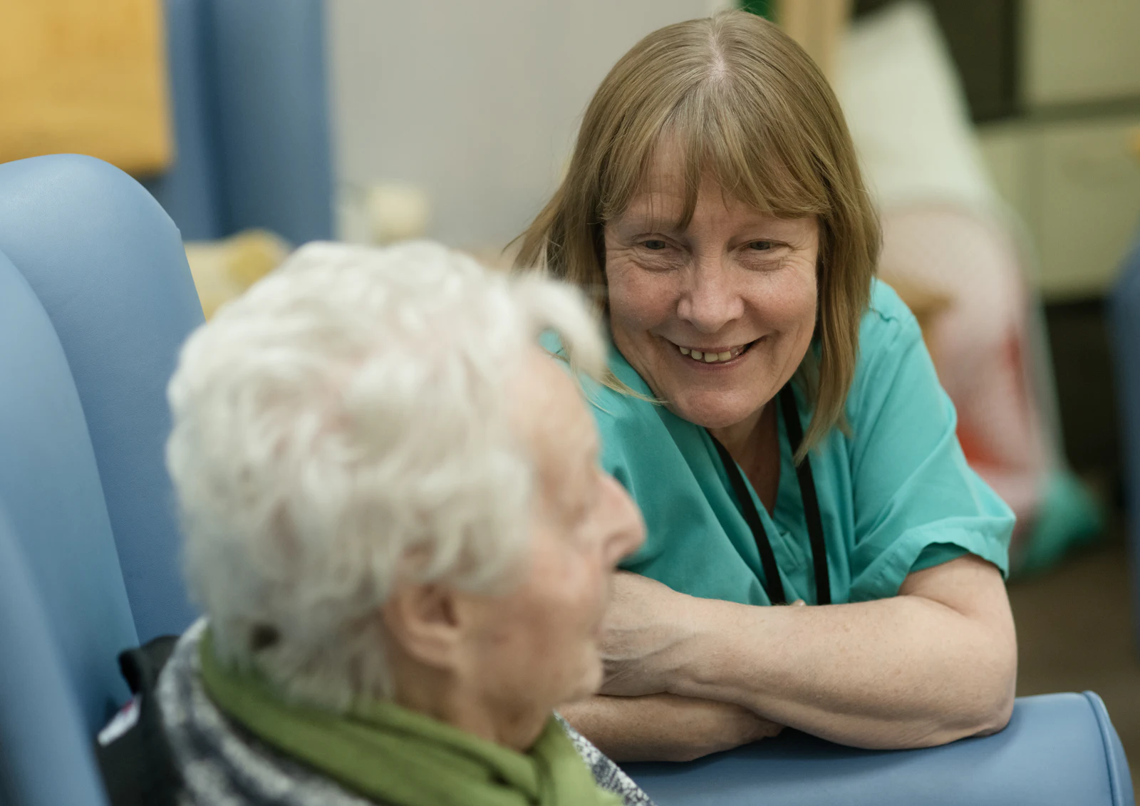 A care worker in green scrubs talking with an older woman